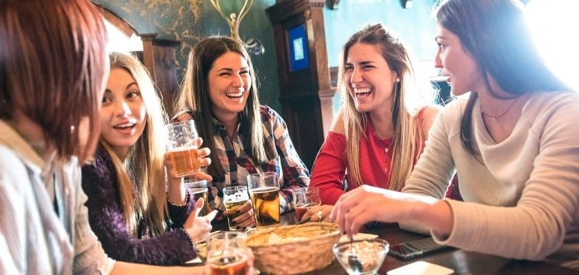 A group of six women laughing and enjoying drinks at a bar.