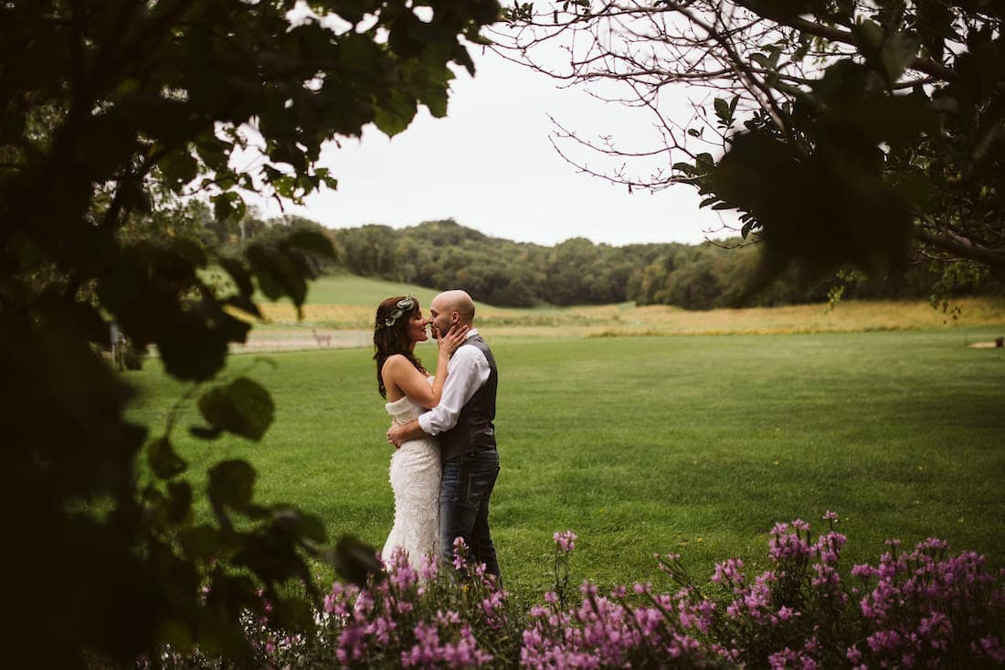 A couple embraces in a lush green field surrounded by flowers.