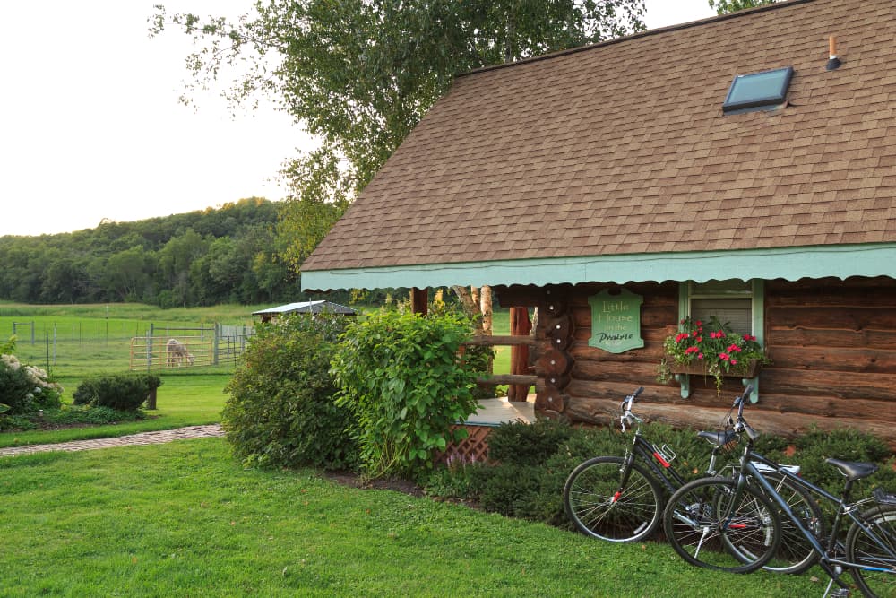 Log cabin with light green scalloped trim looking out into green pasture with gate