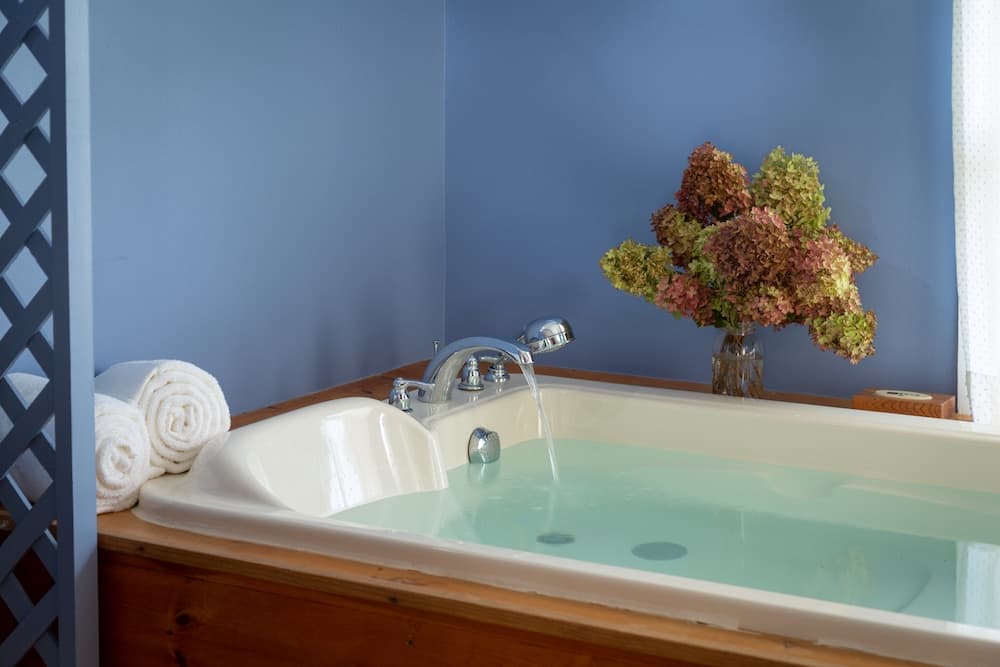 A cozy bathroom features a bathtub filled with water, rolled towels nearby, and a vase of flowers on the windowsill.