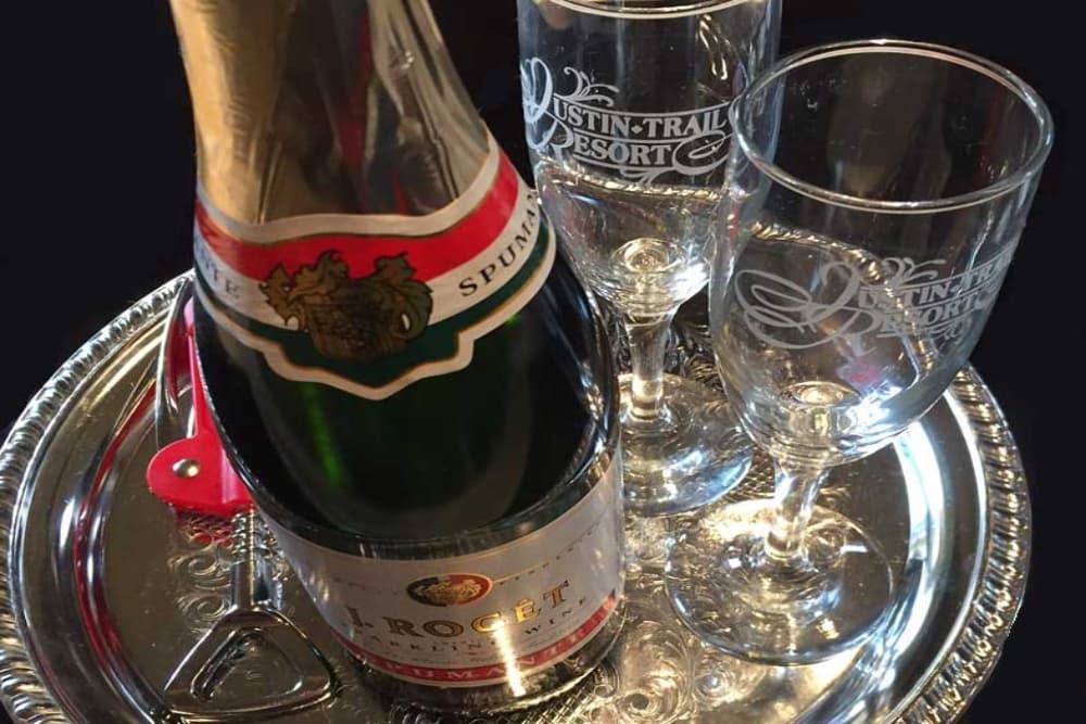 A silver tray with a bottle of red wine, a corkscrew, and 2 Justin Trails wine glasses with their logo etched into them.