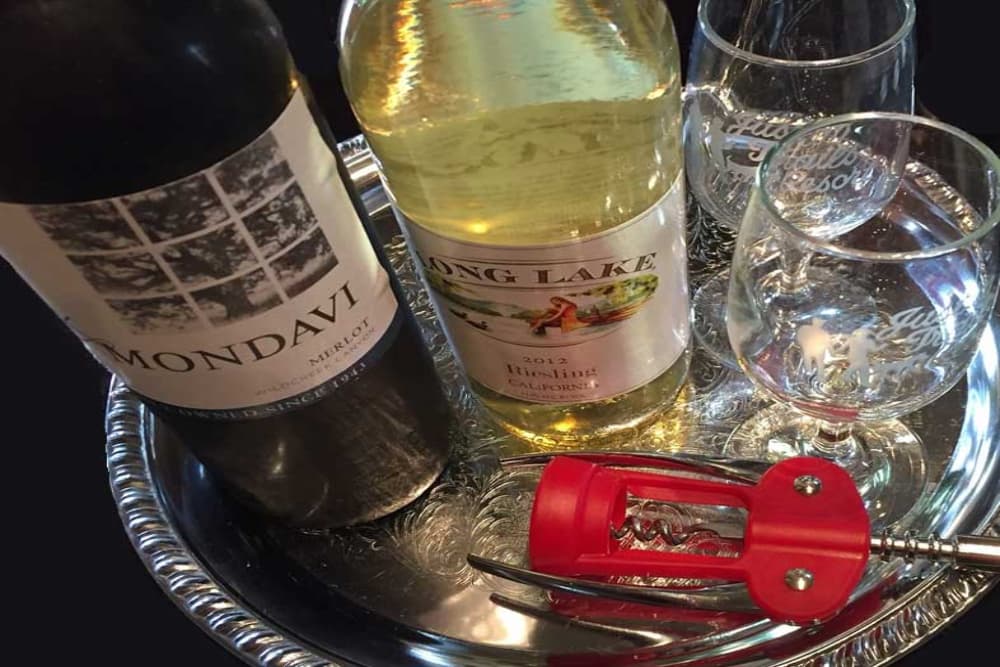 A silver tray with 2 bottles of wine, one red and one white, a corkscrew, and 2 Justin Trails wine glasses with their logo etched into them.