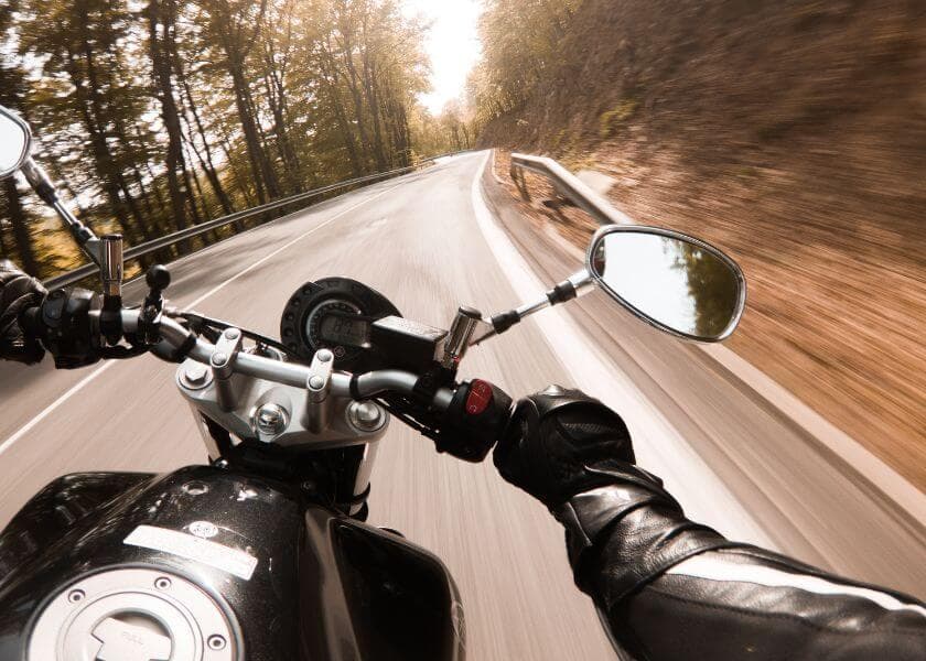 A motorcycle rider accelerates along a winding road surrounded by trees. A motorcycle rider accelerates along a winding road surrounded by trees.