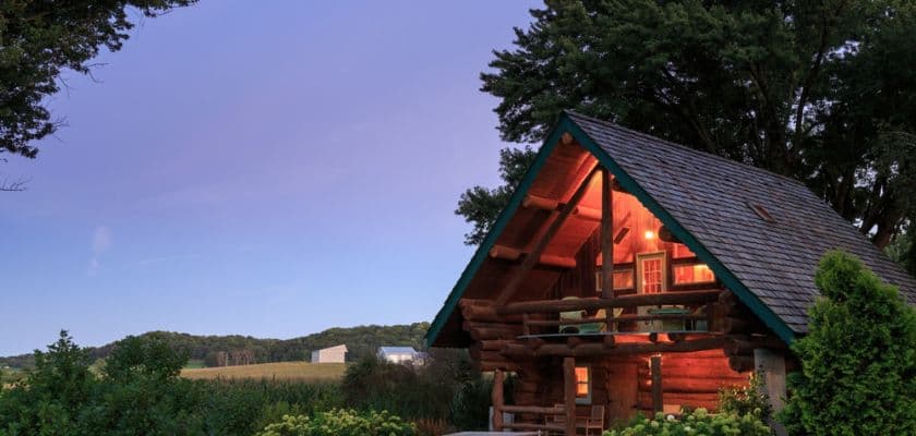 A cozy log cabin surrounded by greenery under a twilight sky.