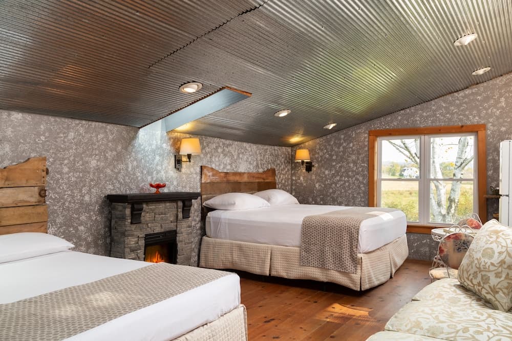 A cozy bedroom featuring two beds, a decorative fireplace, and a large window with a view.