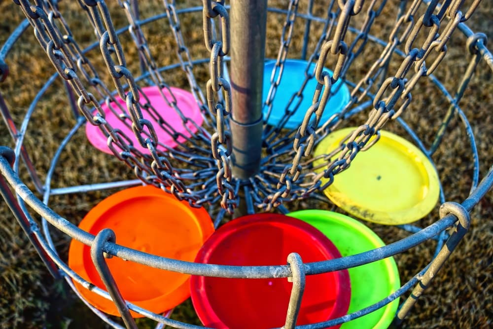 A metal disc golf basket with colorful discs hanging in the chains.