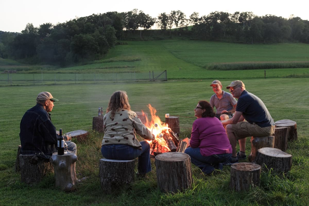 Group of people sitting around a campfire on a grassy field.