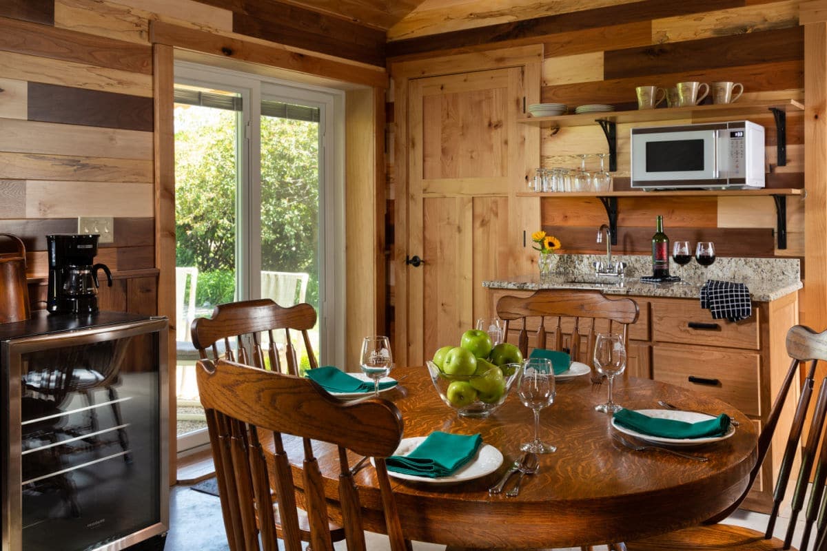 A cozy wooden kitchen featuring a dining table set for four, a granite countertop, and a window overlooking a garden.