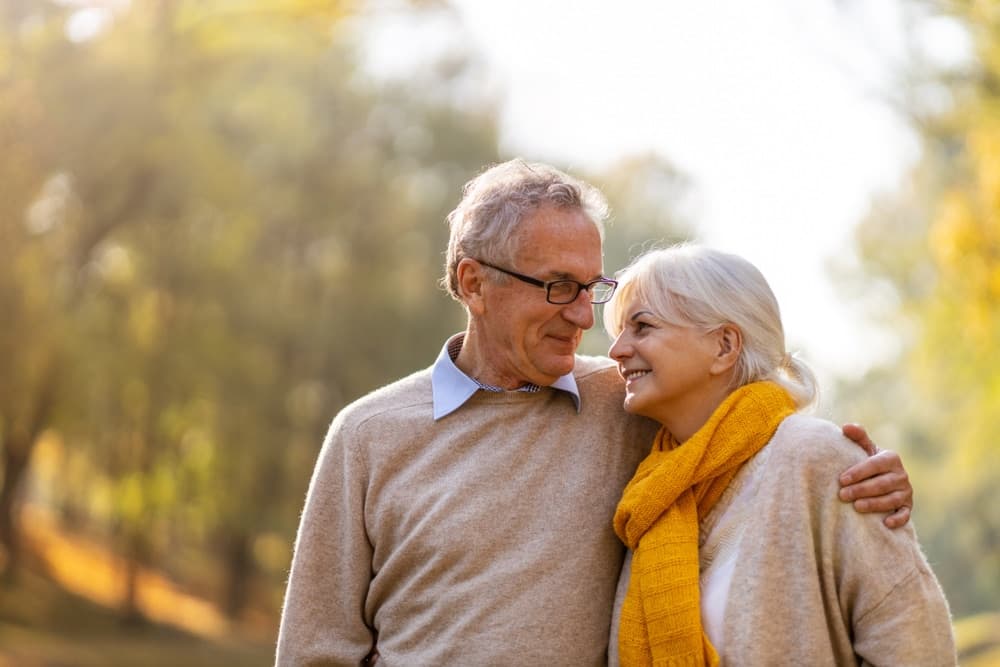 An elderly couple smiles at each other while enjoying a peaceful moment outdoors.