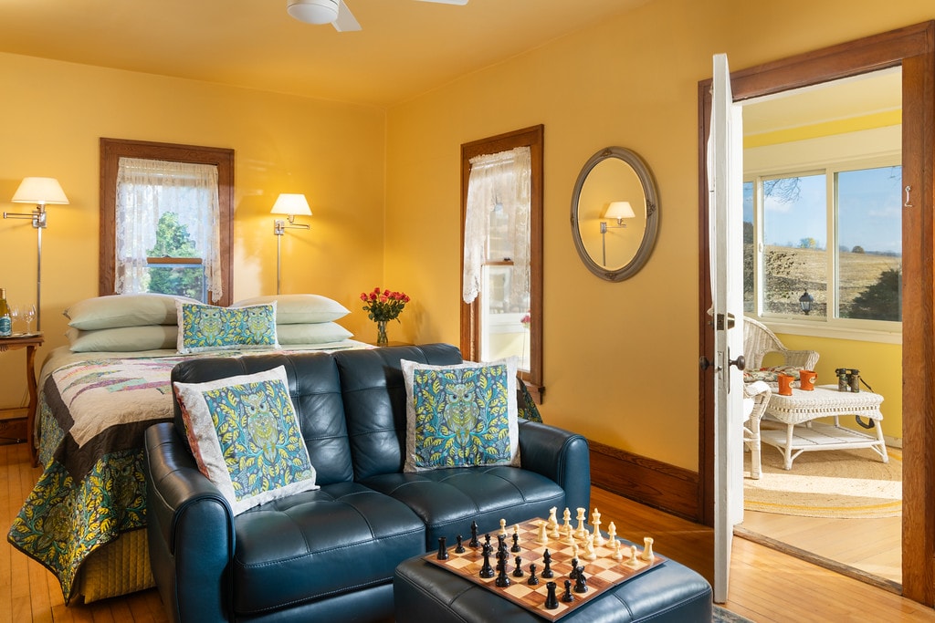 Warm and inviting bedroom with loveseat and ottoman with chess set, and an open door to a private porch