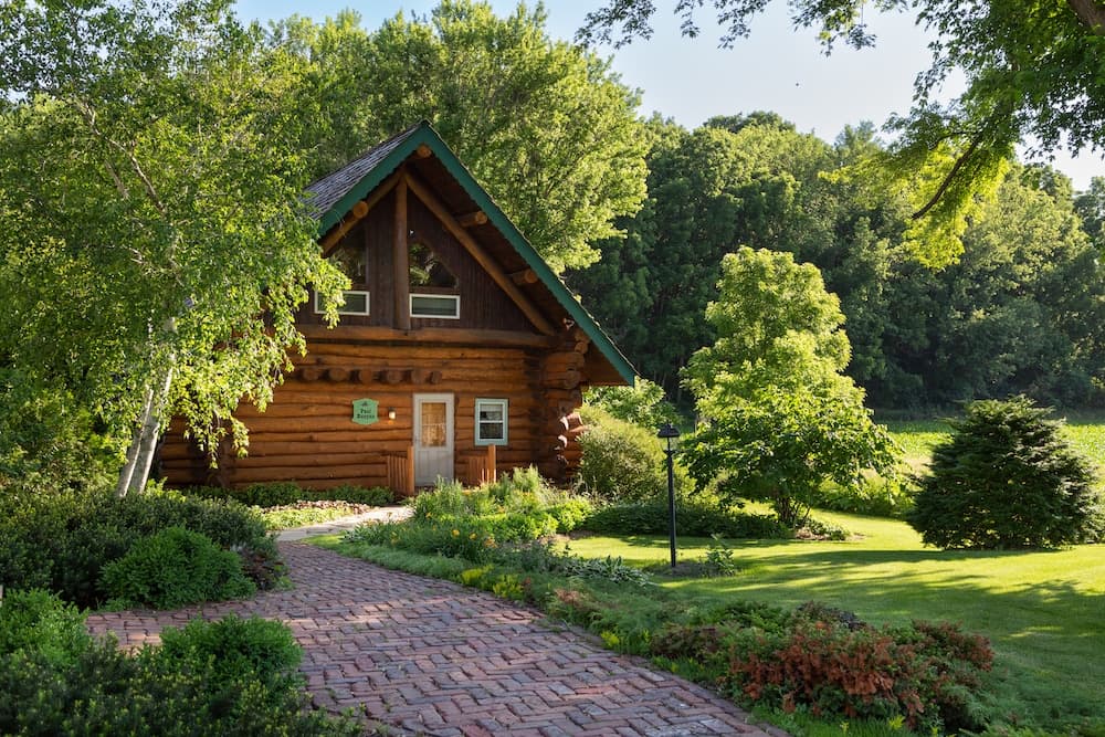 A charming log cabin surrounded by lush greenery and a landscaped pathway.
