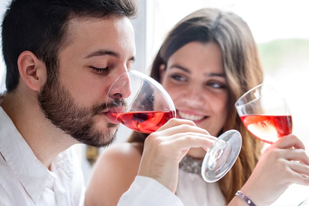 A man and woman toast with glasses of red drink while sharing a moment together. A man and woman toast with glasses of red drink while sharing a moment together.