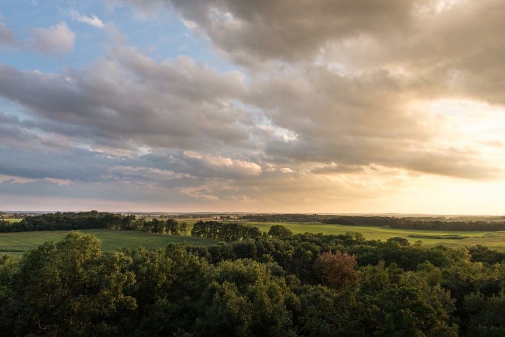 A scenic view of lush green fields under a dramatic sky with clouds at sunset.