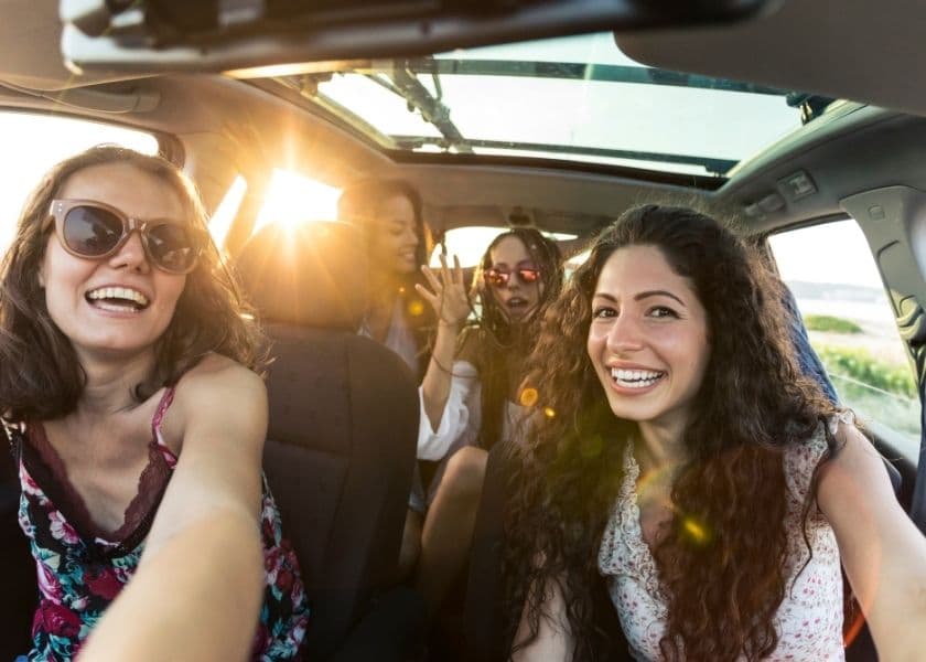Four friends enjoying a sunny car ride, taking a selfie together.