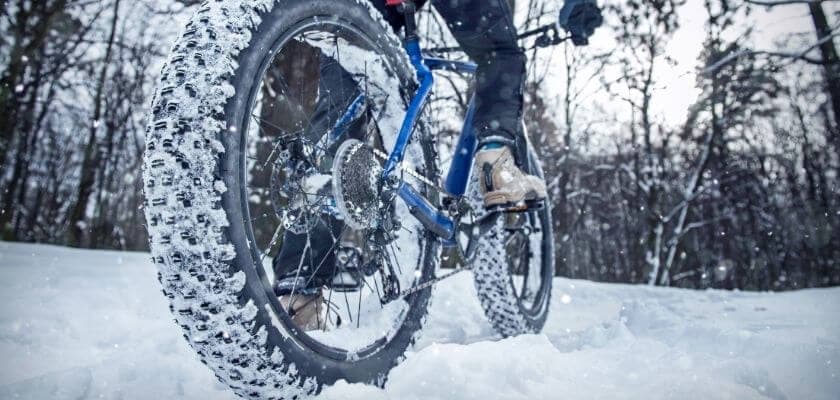 A close-up of a fat tire bike navigating through snow in a forest.