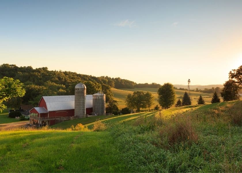 A scenic view of a red barn and silos surrounded by rolling hills at sunset. A scenic view of a red barn and silos surrounded by rolling hills at sunset.