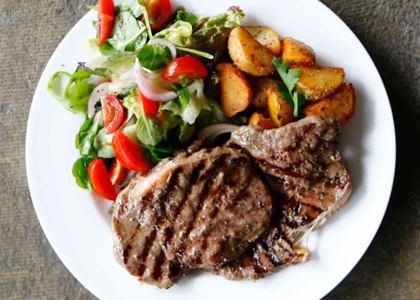 A plate featuring grilled steak, roasted potatoes, and a fresh salad with tomatoes and greens. A plate featuring grilled steak, roasted potatoes, and a fresh salad with tomatoes and greens.