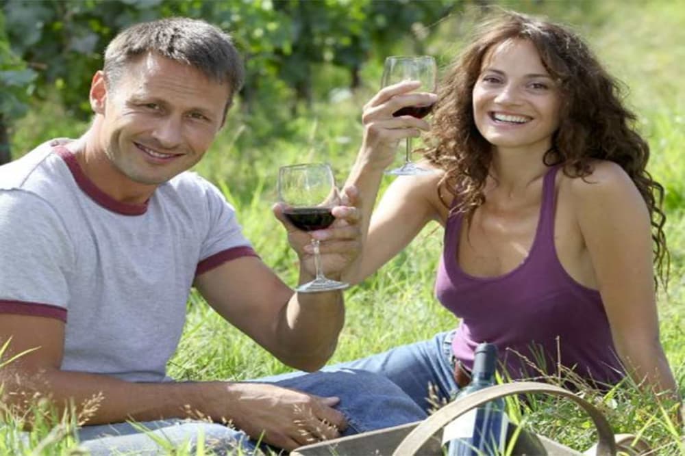 A smiling couple sitting outside enjoying glasses of red wine.