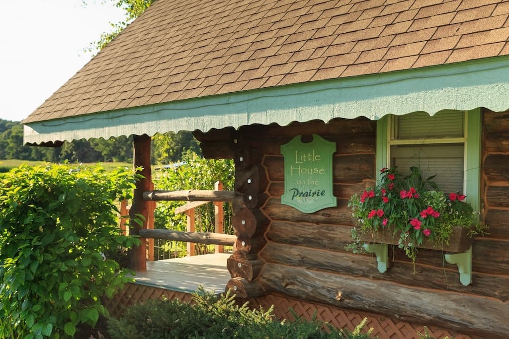 A log cabin with a sign reading "Little House on the Prairie" and colorful flowers on the porch.
