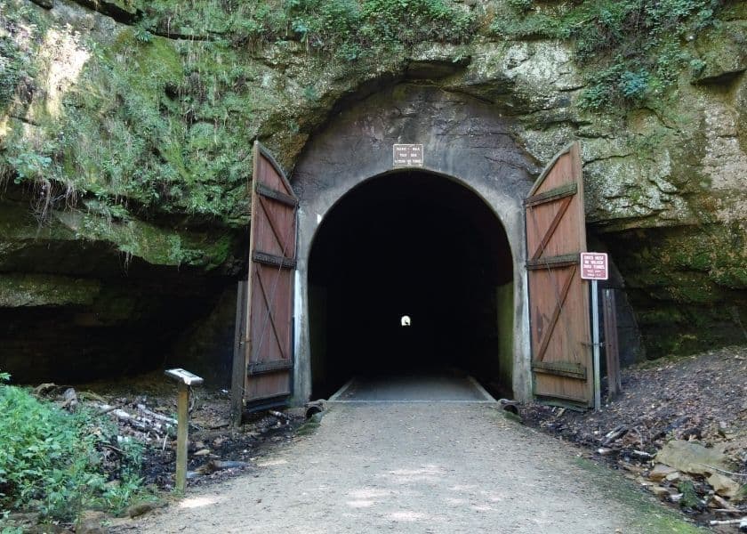 A dark tunnel entrance surrounded by rocky walls and framed by two wooden doors. A dark tunnel entrance surrounded by rocky walls and framed by two wooden doors.