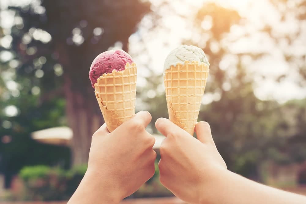 Two hands holding ice cream cones with purple and green scoops.