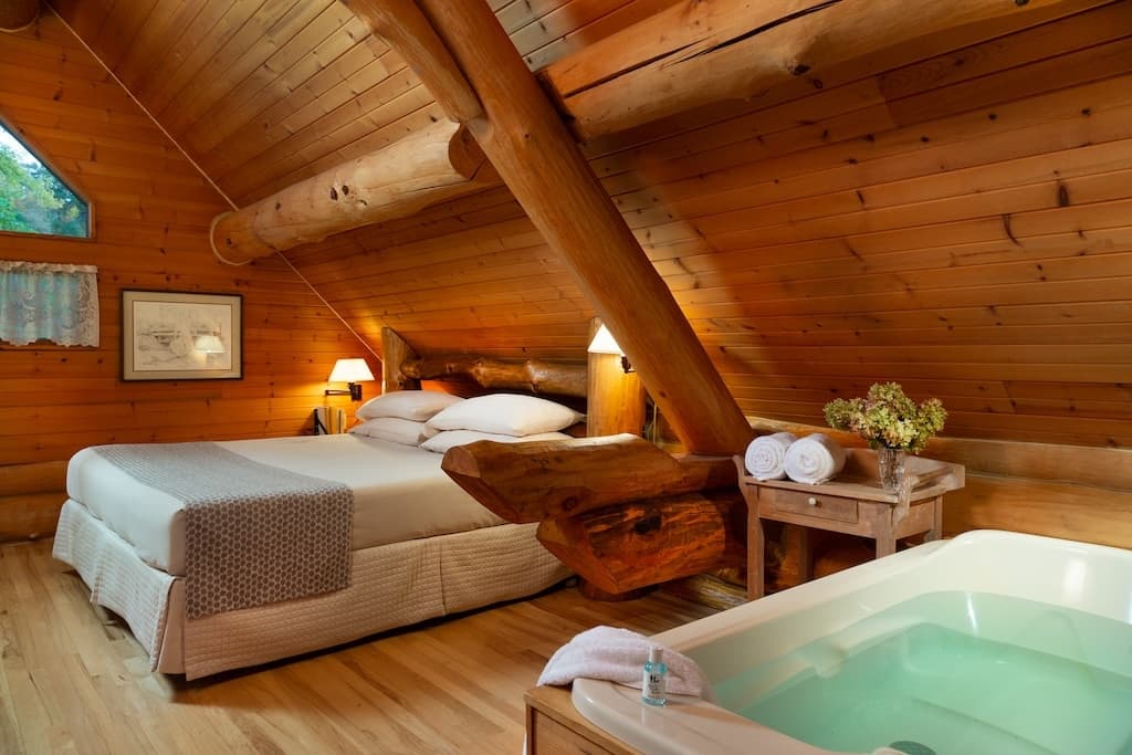 Cozy wooden attic bedroom featuring a large bed, a soaking tub, and rustic decor.