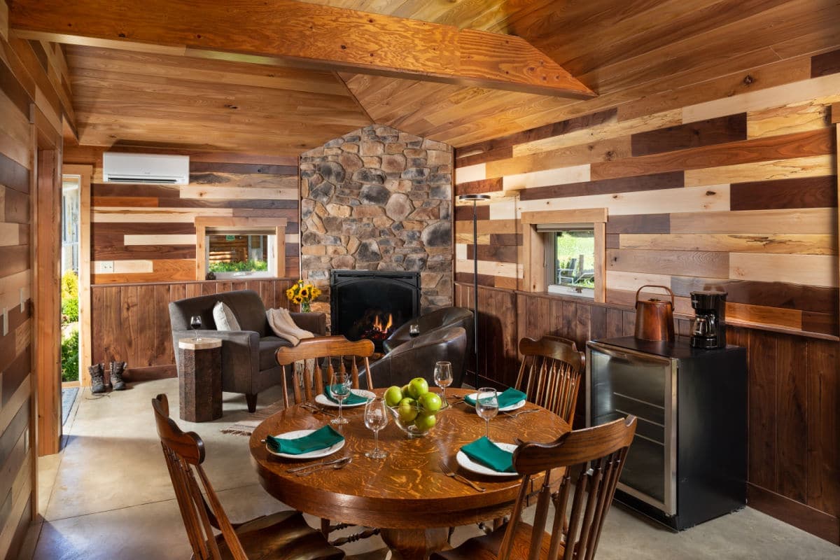 Cozy wooden interior of a cabin featuring a dining table, fireplace, and seating area.