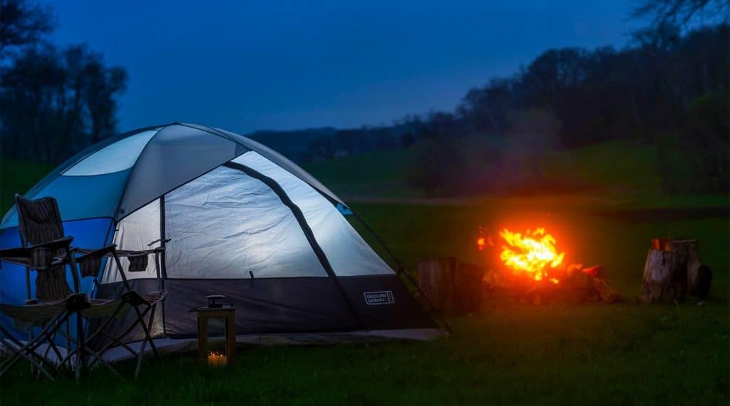 A tent sits by a glowing campfire under a twilight sky.