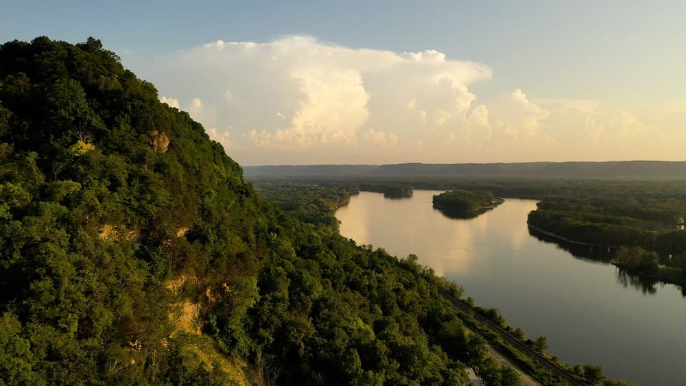 Aerial view of a lush green hillside overlooking a winding river under a cloudy sky.