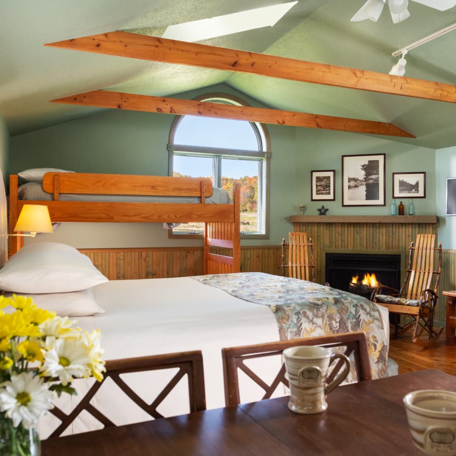 A bedroom with a bed, bunk beds, a table with coffee cups. And a fireplace.