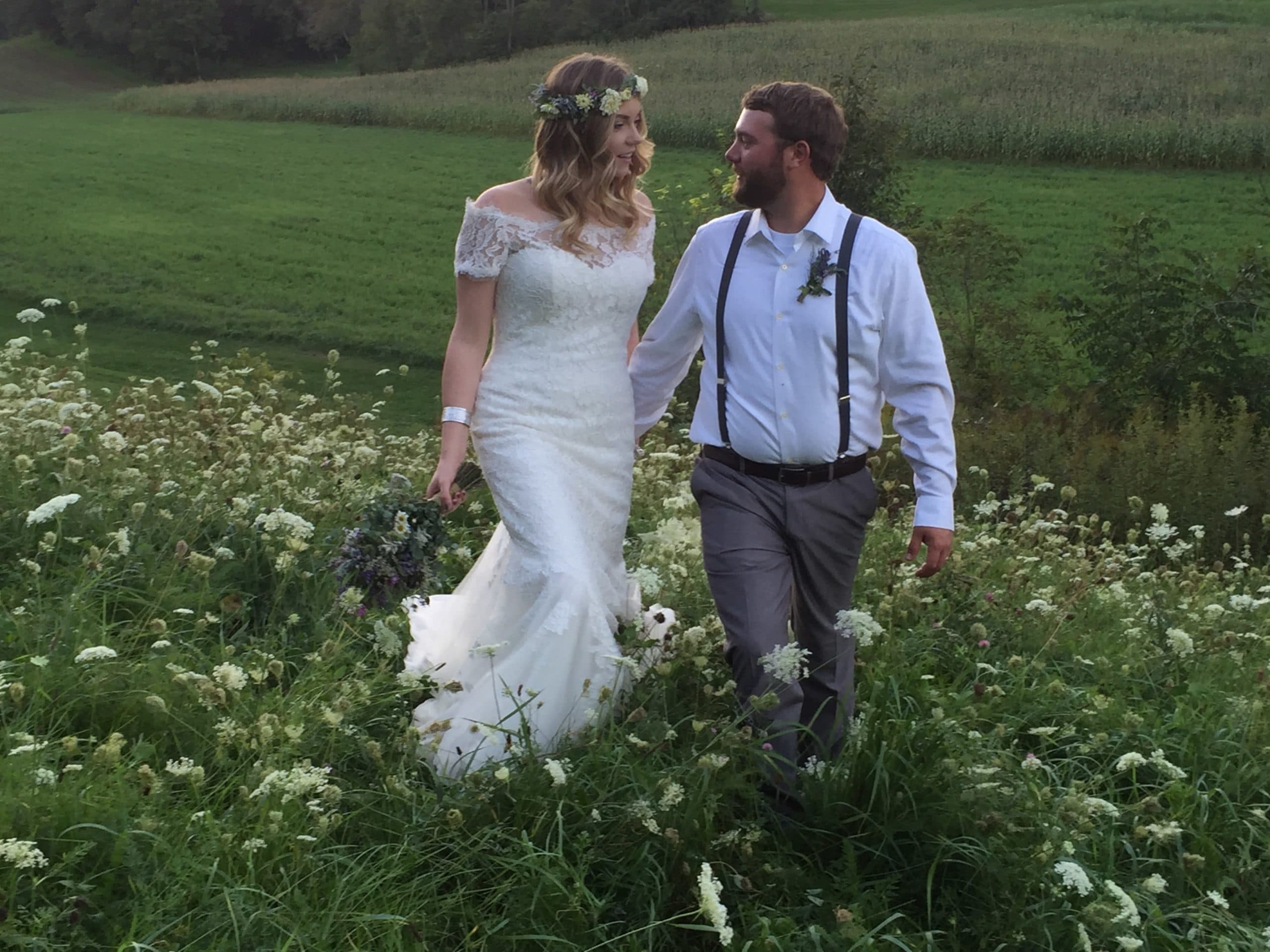 A bride and groom walk hand in hand through a lush field of wildflowers.