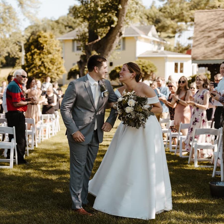 A happy wedding couple walking down the aisle at an outdoor wedding with guests smiling and clapping around them.