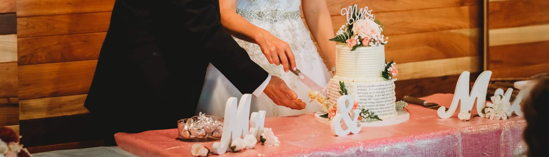 A couple cuts a wedding cake adorned with flowers at their reception.
