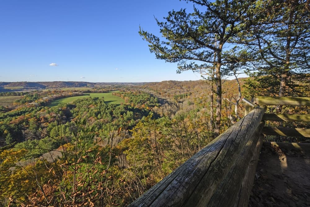 Scenic overlook of a lush valley surrounded by colorful autumn foliage under a clear blue sky.