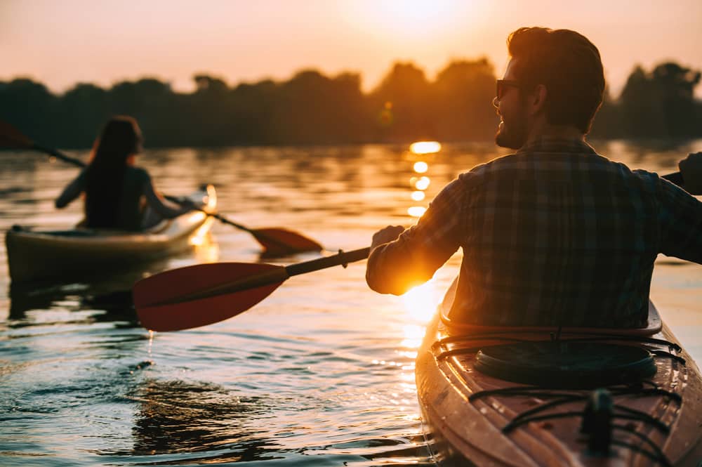 Two people kayaking on a lake during sunset.