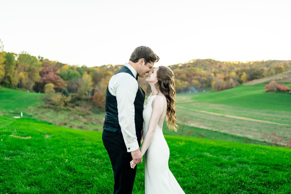 A smiling wedding couple outside in front of a beautiful landscape smiling and touching noses.