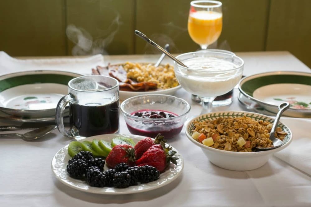 A table set with breakfast foods including fresh fruit, granola, yogurt, scrambled eggs and bacon, coffee, and juice