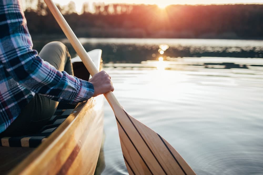 A person paddles a canoe on a serene lake at sunset.