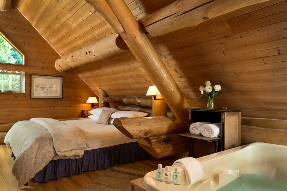 Cozy wooden cabin interior featuring a bed, bathtub, and natural lighting.