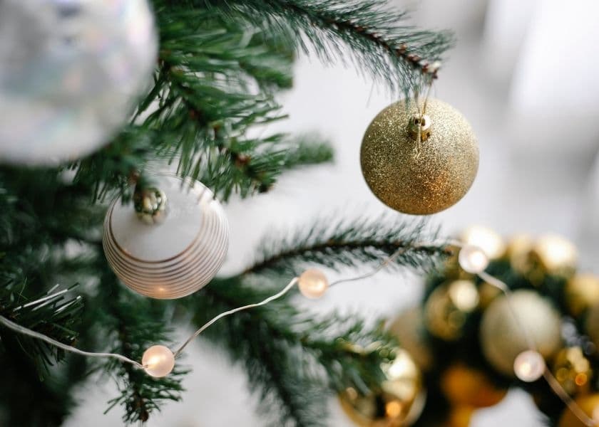 green christmas tree trimmed in string holiday lights and decorative bulbs with a blurred white backdrop green christmas tree trimmed in string holiday lights and decorative bulbs with a blurred white backdrop