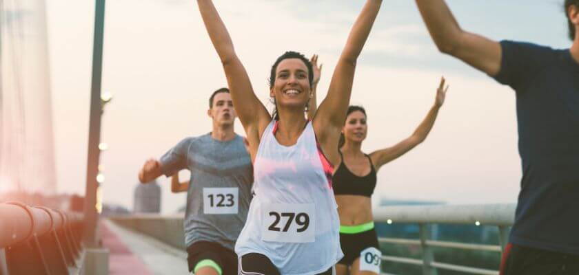 group of marathon runners with race bibs celebrating as they run across a bridge at sunrise or sunset.