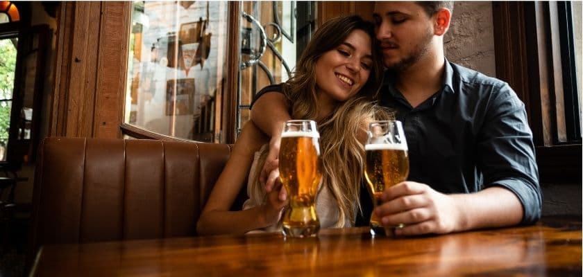 a couple snuggled close in a booth holding glasses of beer